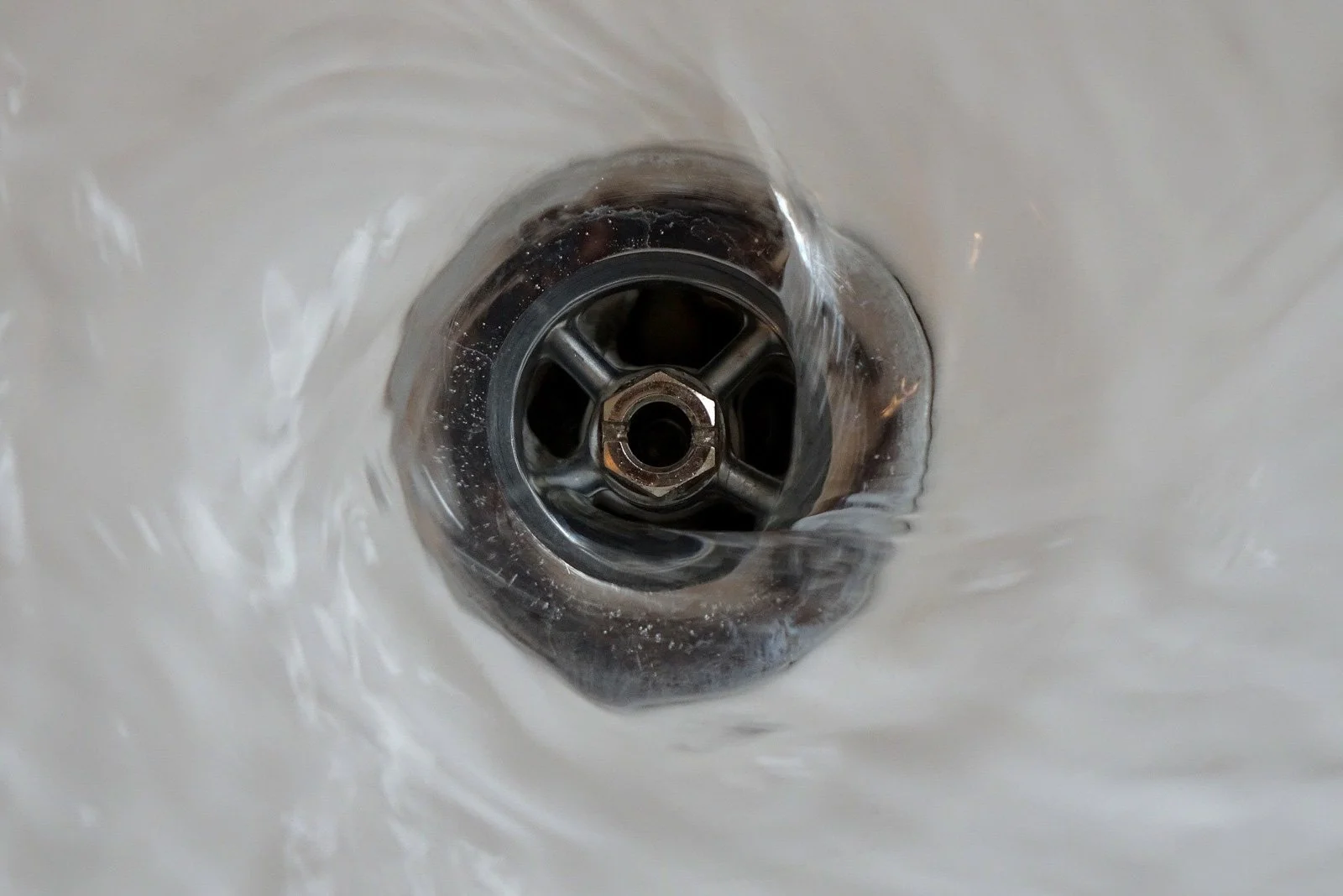 Close-up of water swirling around a metal drain in a white sink, highlighting the need for expert Drain Cleaning. Perfect for illustrating professional Drain Service in Brea California.