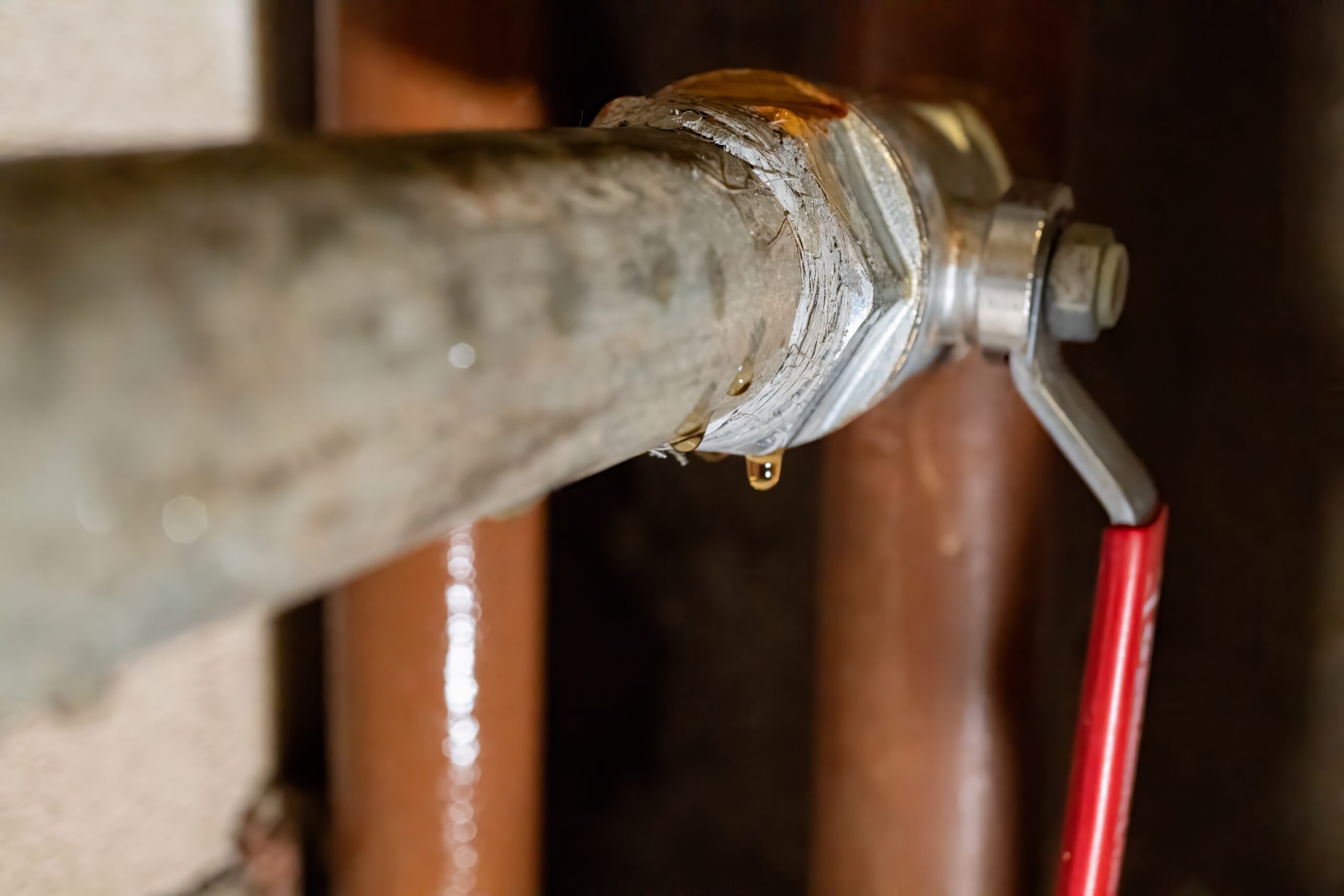 Close-up of a metal pipe with a shut-off valve, showing a small leak where water drips from a joint—one of the common pipe leak signs or an indication of a hidden pipe leak.