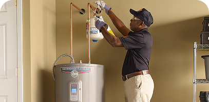 A technician wearing gloves and a cap is performing maintenance on a water heater with copper pipes in a utility room.