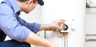 Person in a blue shirt and cap adjusts the settings on a water heater unit, focusing on the control panel.