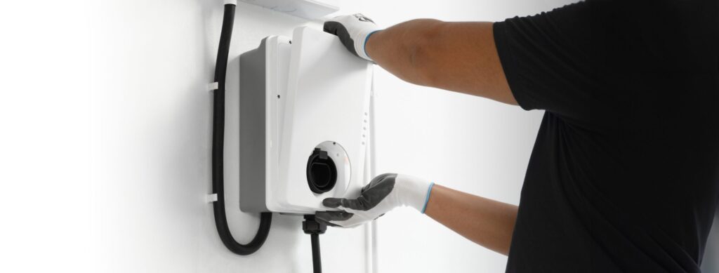A person wearing gloves installs or maintains a white EV charger on a white wall, highlighting professional EV charger installations ideal for homeowners in Brea.