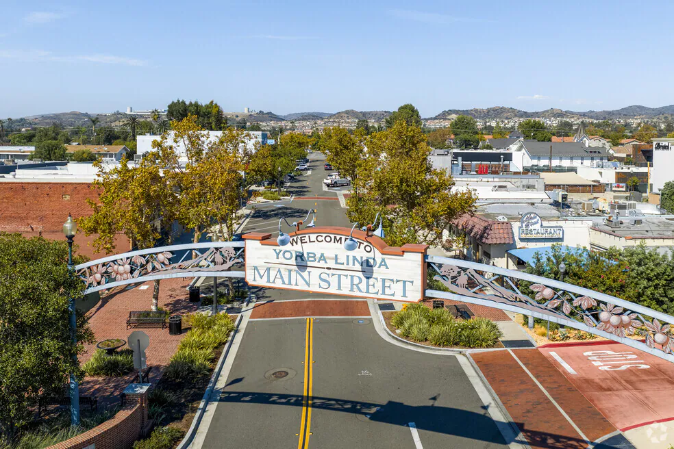 A large arching sign reads "Welcome to Yorba Linda Main Street" over an empty street lined with trees and buildings under a clear Orange County, California sky.