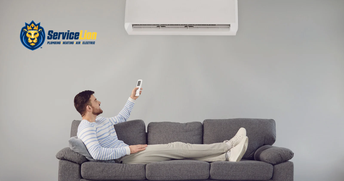 A man on a sofa uses a remote to adjust a wall-mounted air conditioner to manage high energy costs. The ServiceLion logo is in the top left corner.